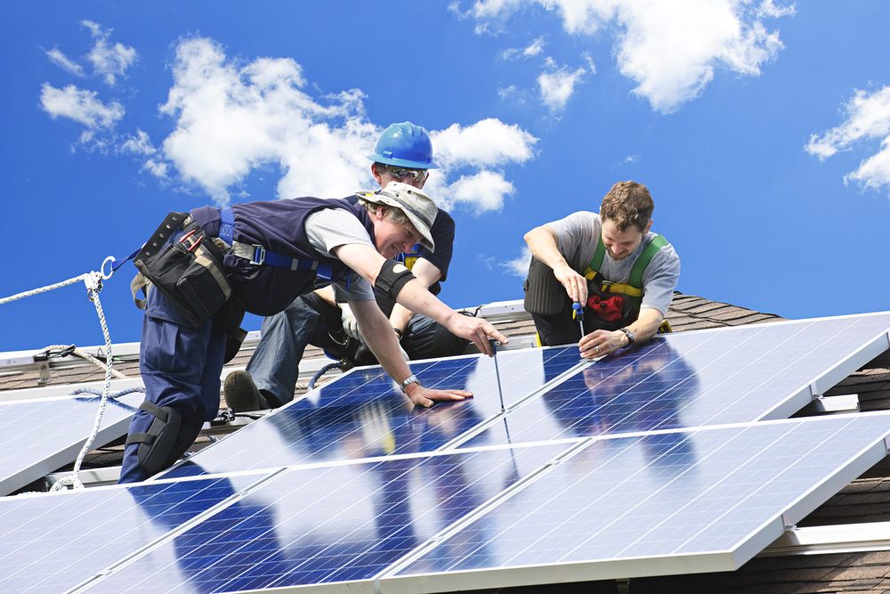 Dělníci instalují photovoltaické solární panely na střechu